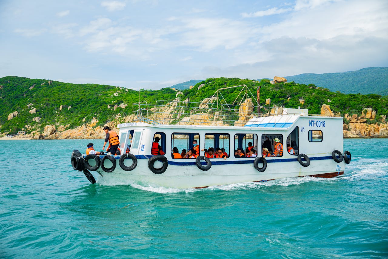 A boat filled with tourists in life jackets traverses vibrant turquoise waters along a lush, green coastline.